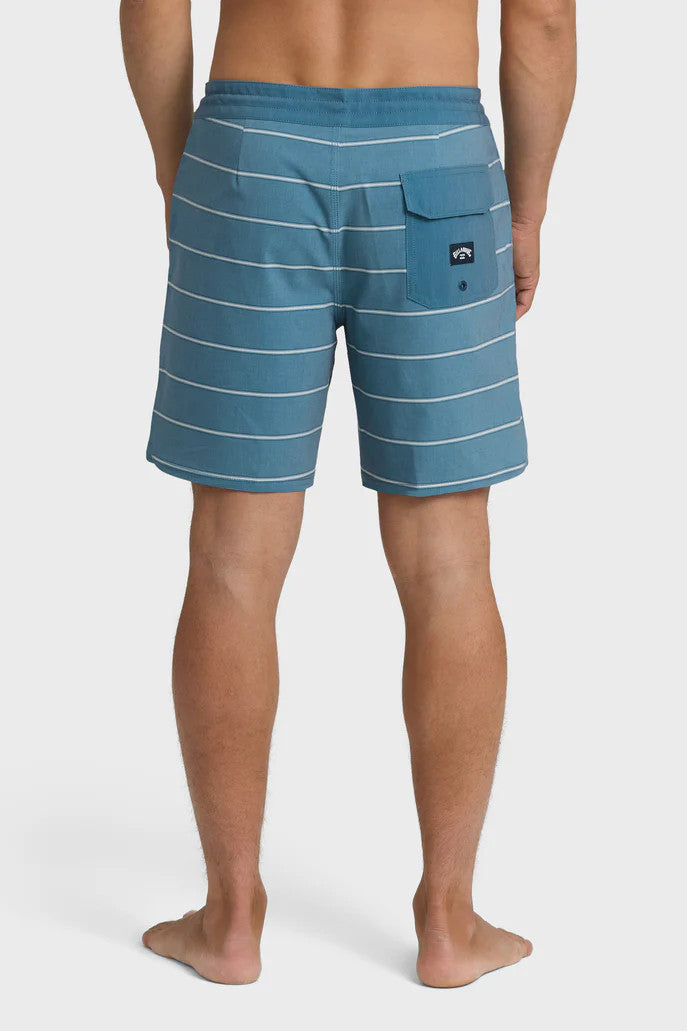 Back view of a  man wearing blue boardshorts with white stripes and a drawstring waist on a white background.