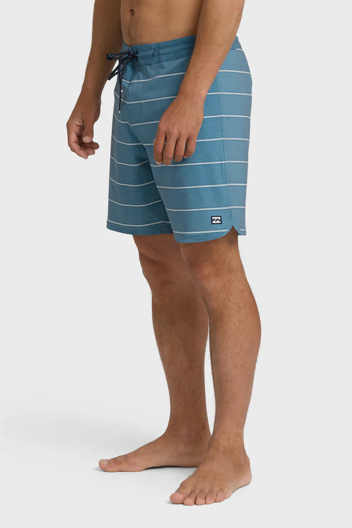 A man wearing blue boardshorts with white stripes and a drawstring waist on a white background.