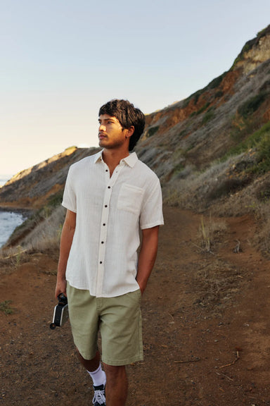 Man in a white button up shirt standing on a coastal path walking near the water