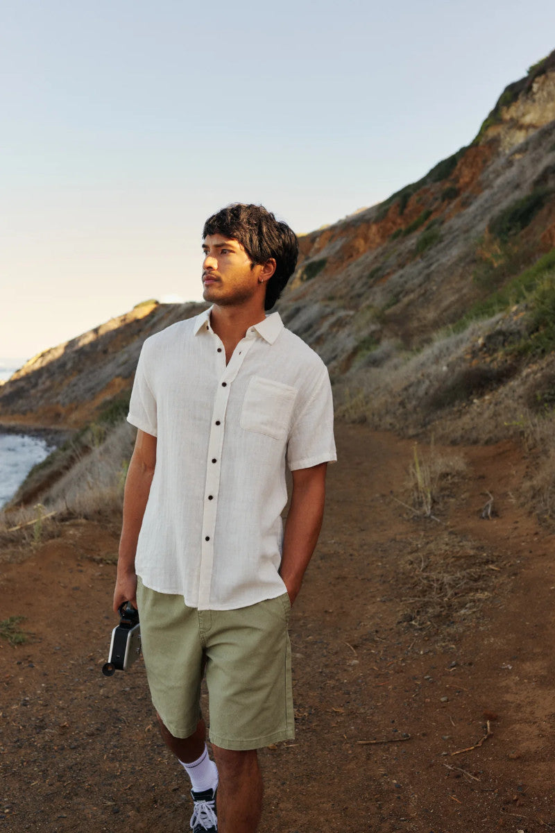 Man in a white button up shirt standing on a coastal path walking near the water