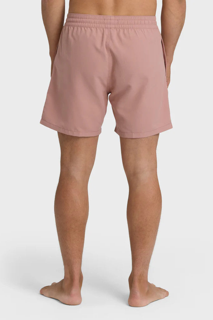 Back view of a man standing and posing in a pair of rose pink boardshorts with a side pocket, featuring an elastic waist closure.