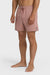 A man standing and posing in a pair of rose pink boardshorts with a side pocket, featuring an elastic waist closure.