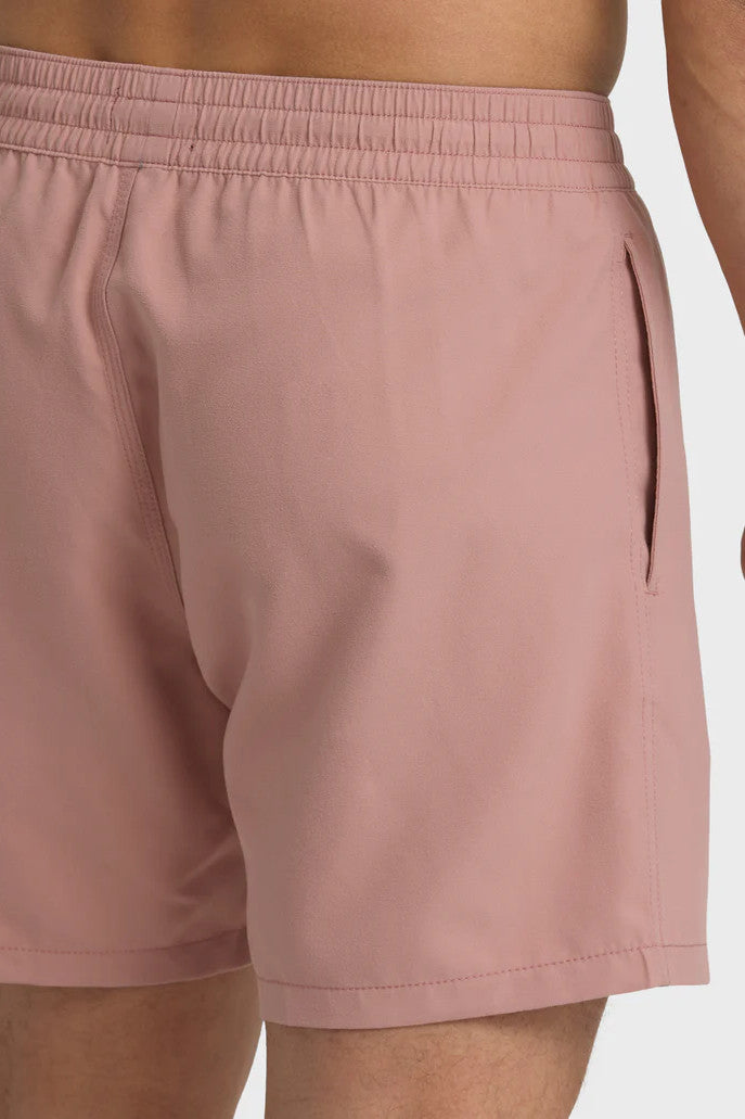 A man standing and posing in a pair of rose pink boardshorts with a side pocket, featuring an elastic waist closure.