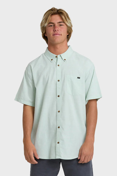 Man wearing a solid, light green short-sleeve button-up collared shirt on a white background