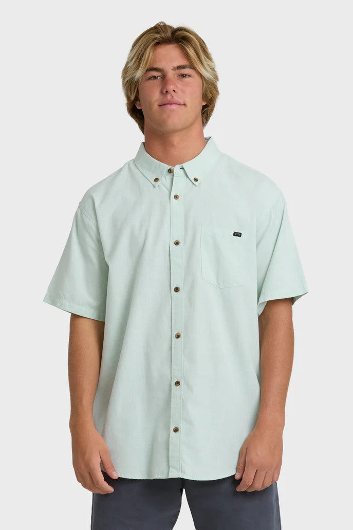 Man wearing a solid, light green short-sleeve button-up collared shirt on a white background