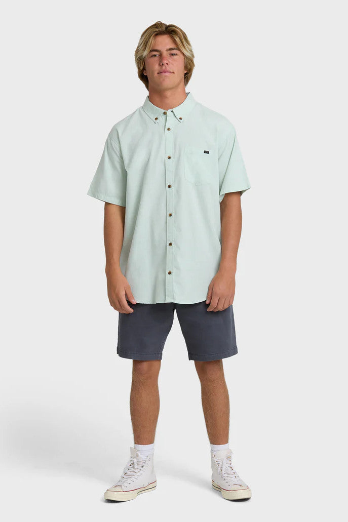 Man wearing a solid, light green short-sleeve button-up collared shirt and navy shorts on a white background