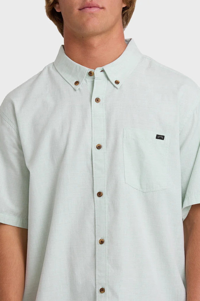 Man wearing a solid, light green short-sleeve button-up collared shirt on a white background