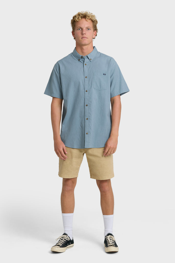 Man wearing a solid, blue short-sleeve button-up collared shirt on a white background