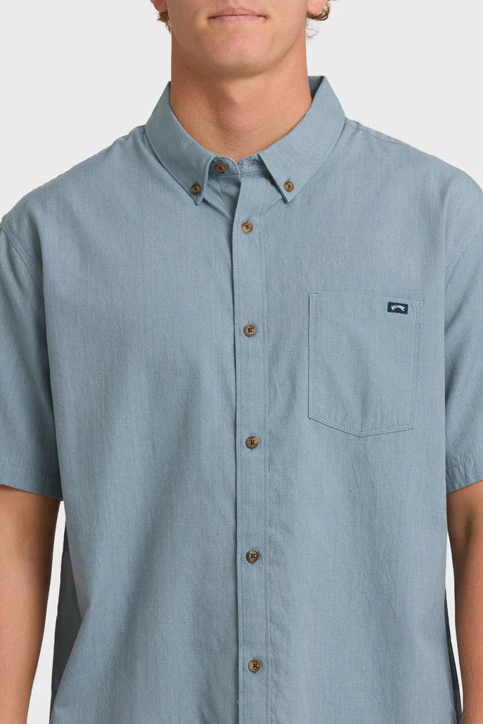 Man wearing a solid, blue short-sleeve button-up collared shirt on a white background