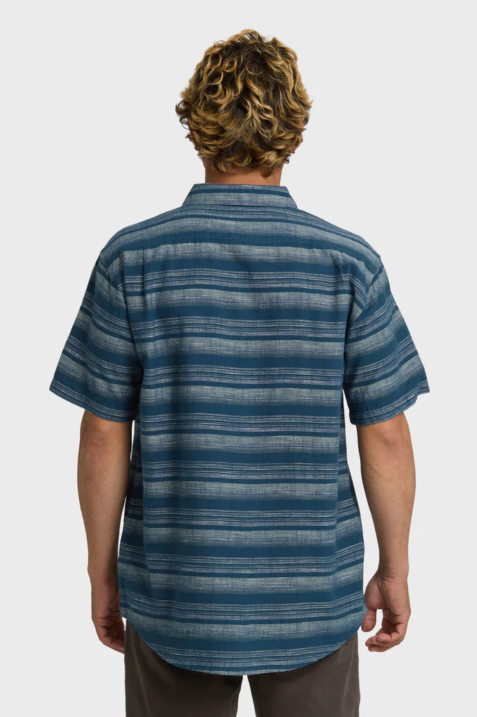 Back view of a man wearing a striped short-sleeved woven shirt with a collar and button-up closure, featuring a chest pocket. The shirt is primarily dark blue with faded cream stripes.
