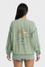 Person wearing a green sweatshirt with 'Tropical Days and Nights' design on the back, standing against a white background.