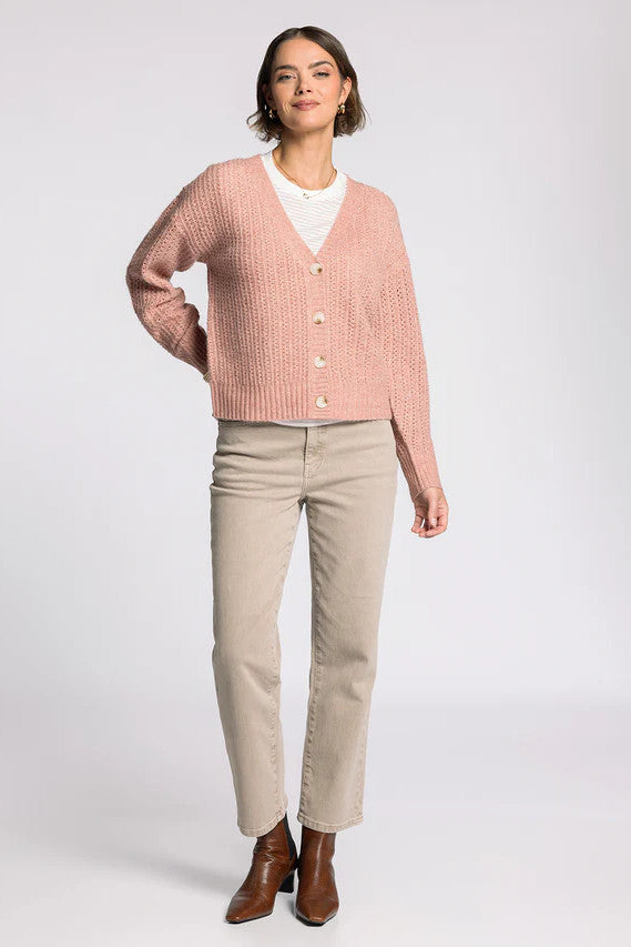 Woman wearing a pink cardigan, white shirt, beige pants, and brown boots on a white background