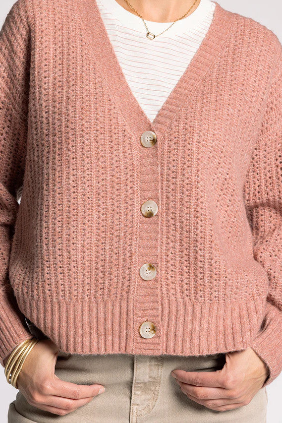 Woman wearing a pink cardigan, white shirt, and beige pants on a white background