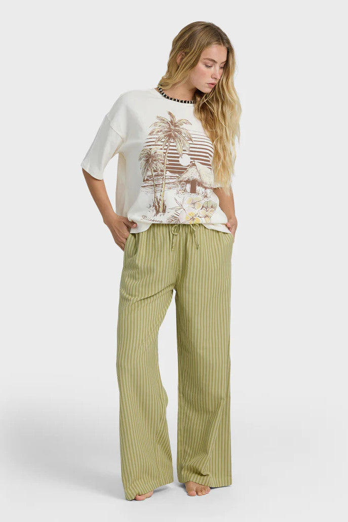 Woman wearing a white top with a palm tree design and green striped pants on a white background