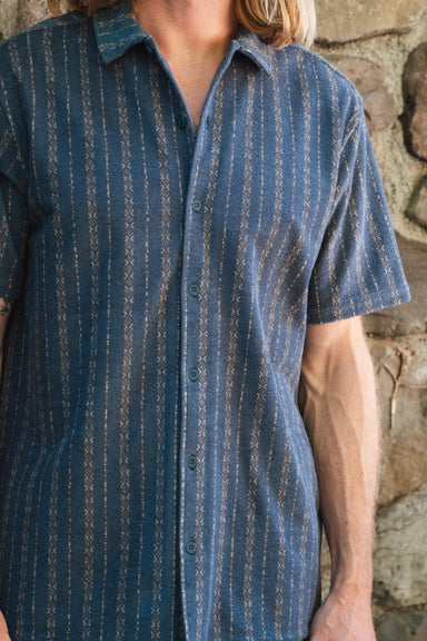 Man wearing a short-sleeve shirt with a subtle pattern on a stone background