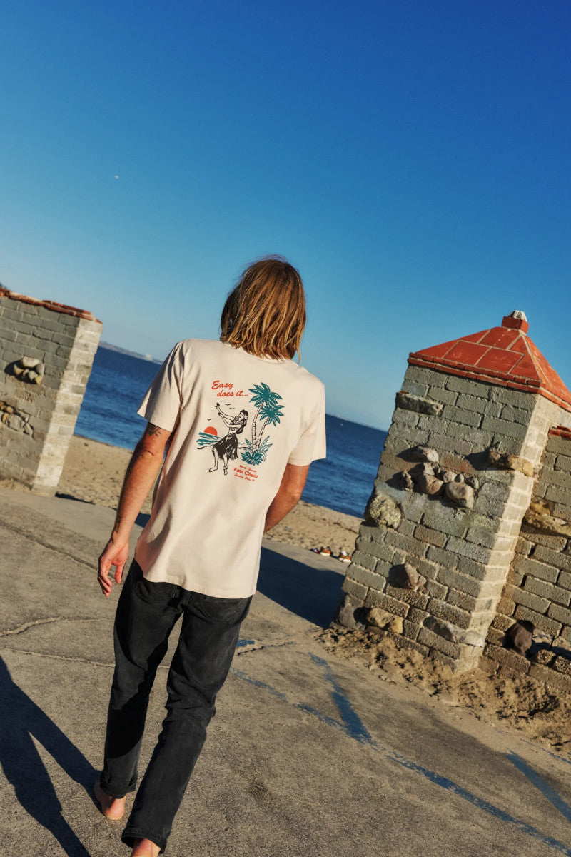 Person walking on a path by a body of water with stone structures and clear blue sky.