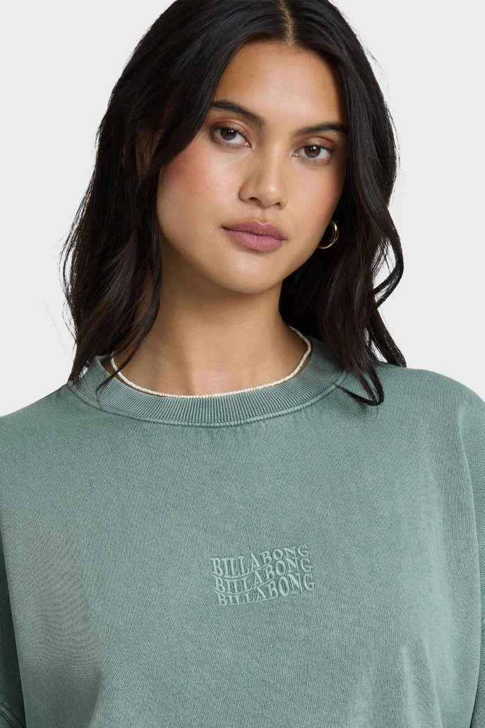 Woman wearing a blue-green sweatshirt with a tonal logo on a white background
