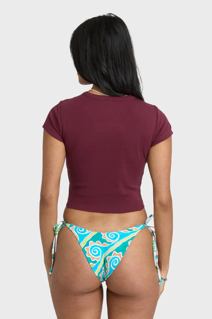 Woman wearing a maroon graphic t-shirt and colorful bikini bottom on a white background