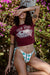 Woman wearing a maroon graphic t-shirt and colorful bikini bottom in a natural setting with greenery and flowers.