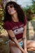 Woman wearing a maroon graphic t-shirt and colorful bikini bottom in a natural setting with greenery and flowers.