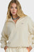 Woman wearing a beige tracksuit with a brand logo on a white background