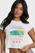 Woman wearing a white graphic t-shirt that says "the art of collecting seashells" and checkered shorts on a white background