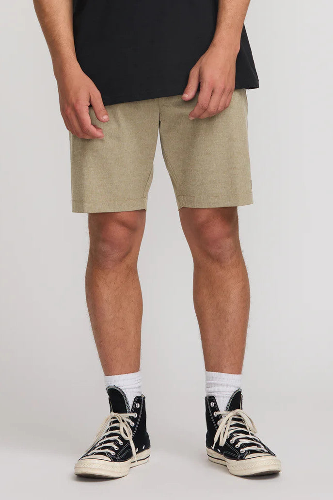 Person wearing beige shorts and black high-top sneakers on a plain background