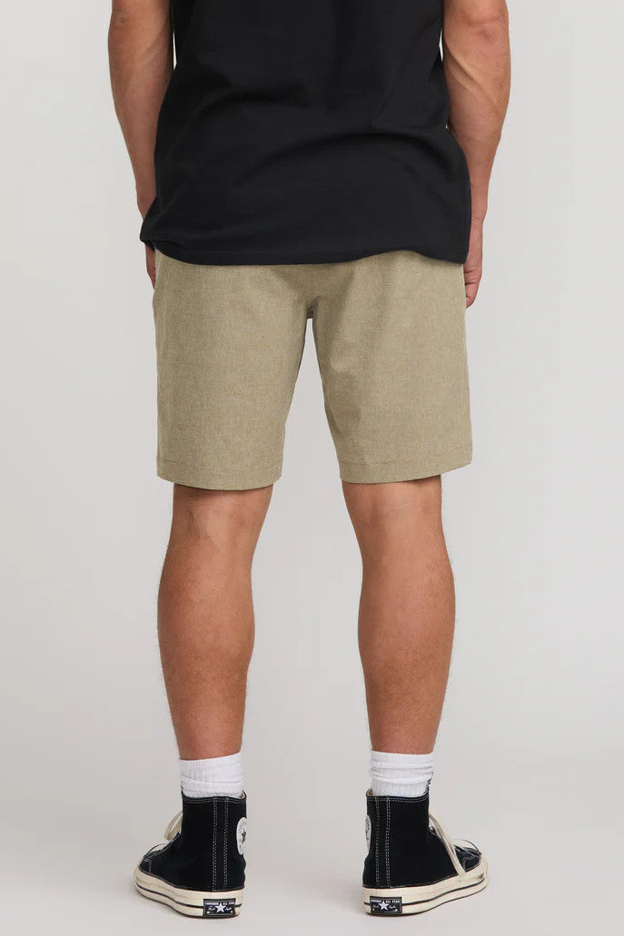 Person wearing beige shorts and black sneakers on a plain background