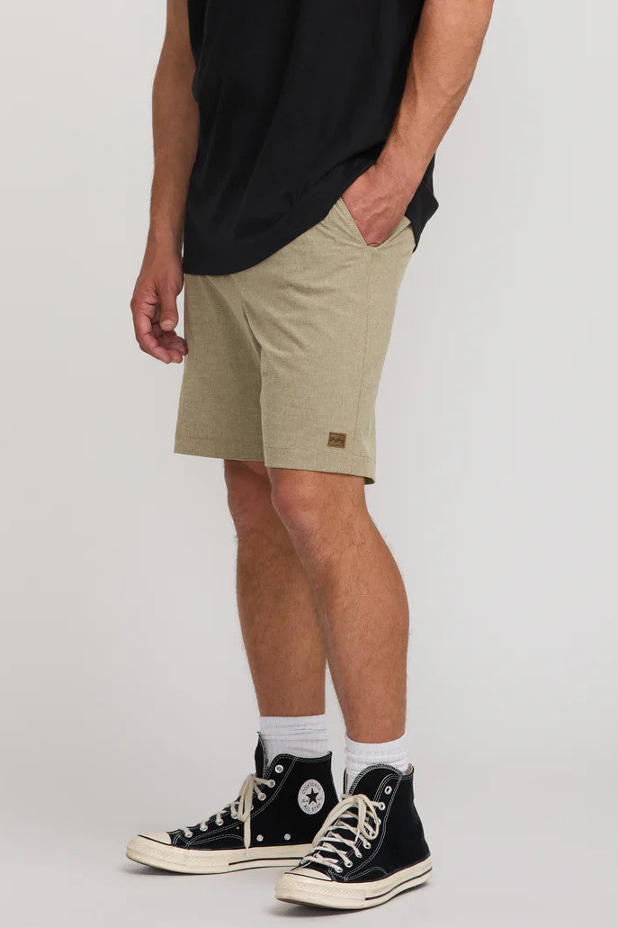 Person wearing beige shorts and black Converse shoes on a white background