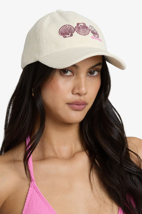 Woman wearing a beige cap with shell designs on a white background