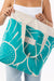 Person holding a teal tote bag with white floral design and 'Aloha' branding.