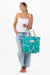 Woman holding a teal tote bag with leaf design on a white background