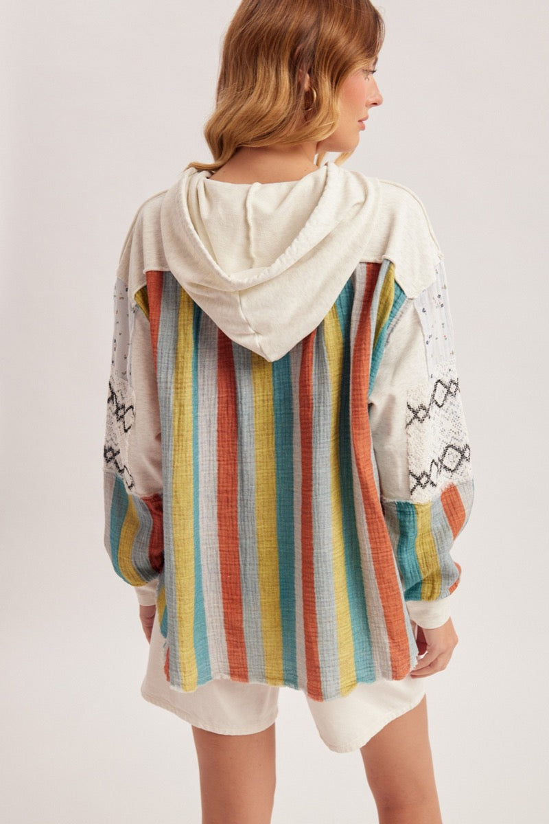 Person wearing a colorful striped hoodie with a white hood on a plain background