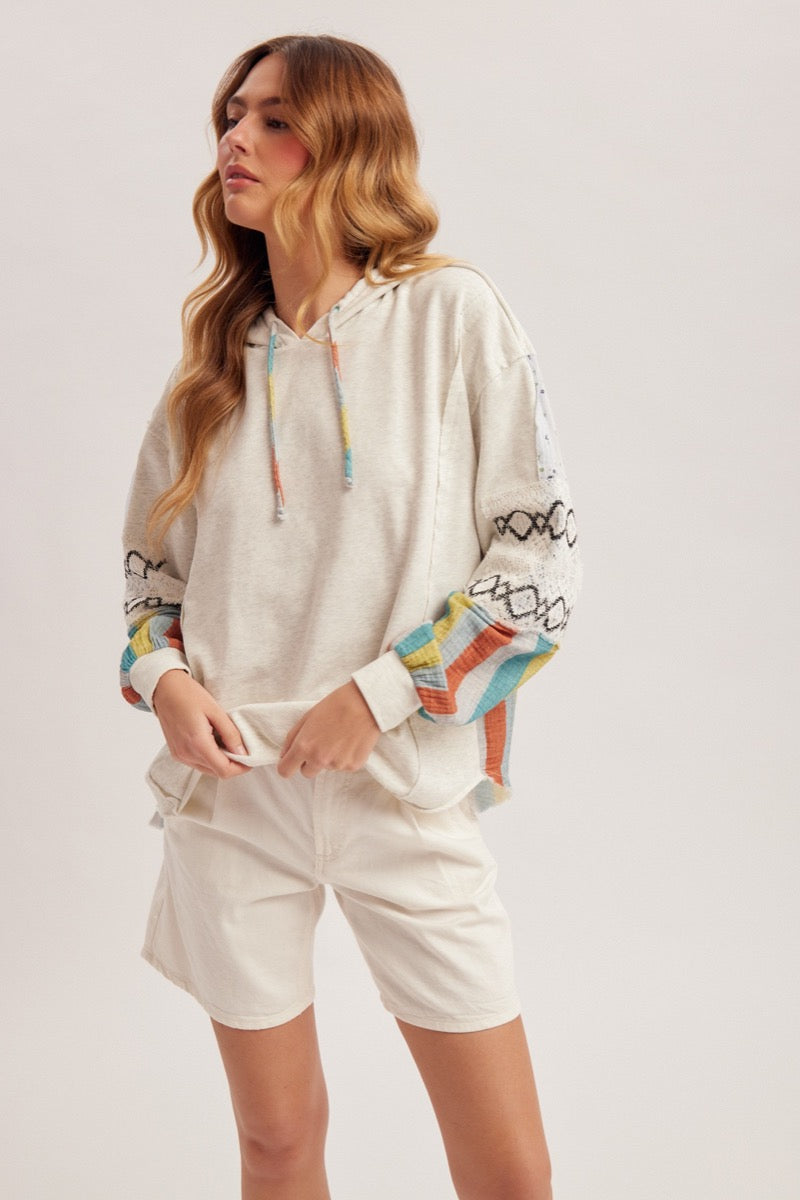 Woman wearing an oatmeal hoodie with colorful designs and white shorts on a plain background