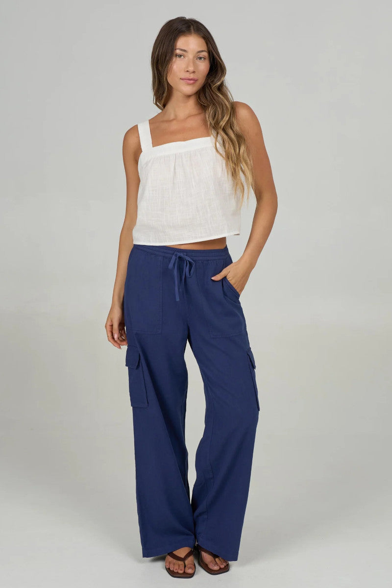 Woman wearing a white top and blue cargo pants on a plain background