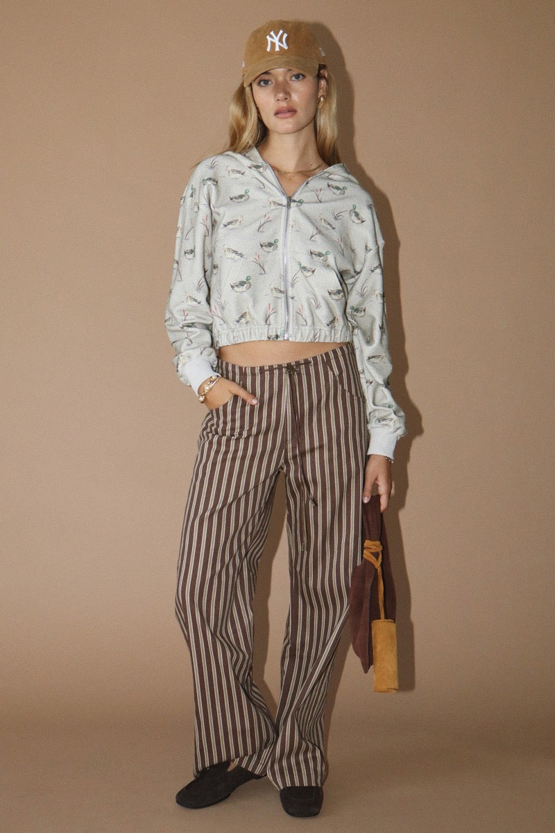 Woman wearing a duck patterned hoodie and striped pants against a beige background