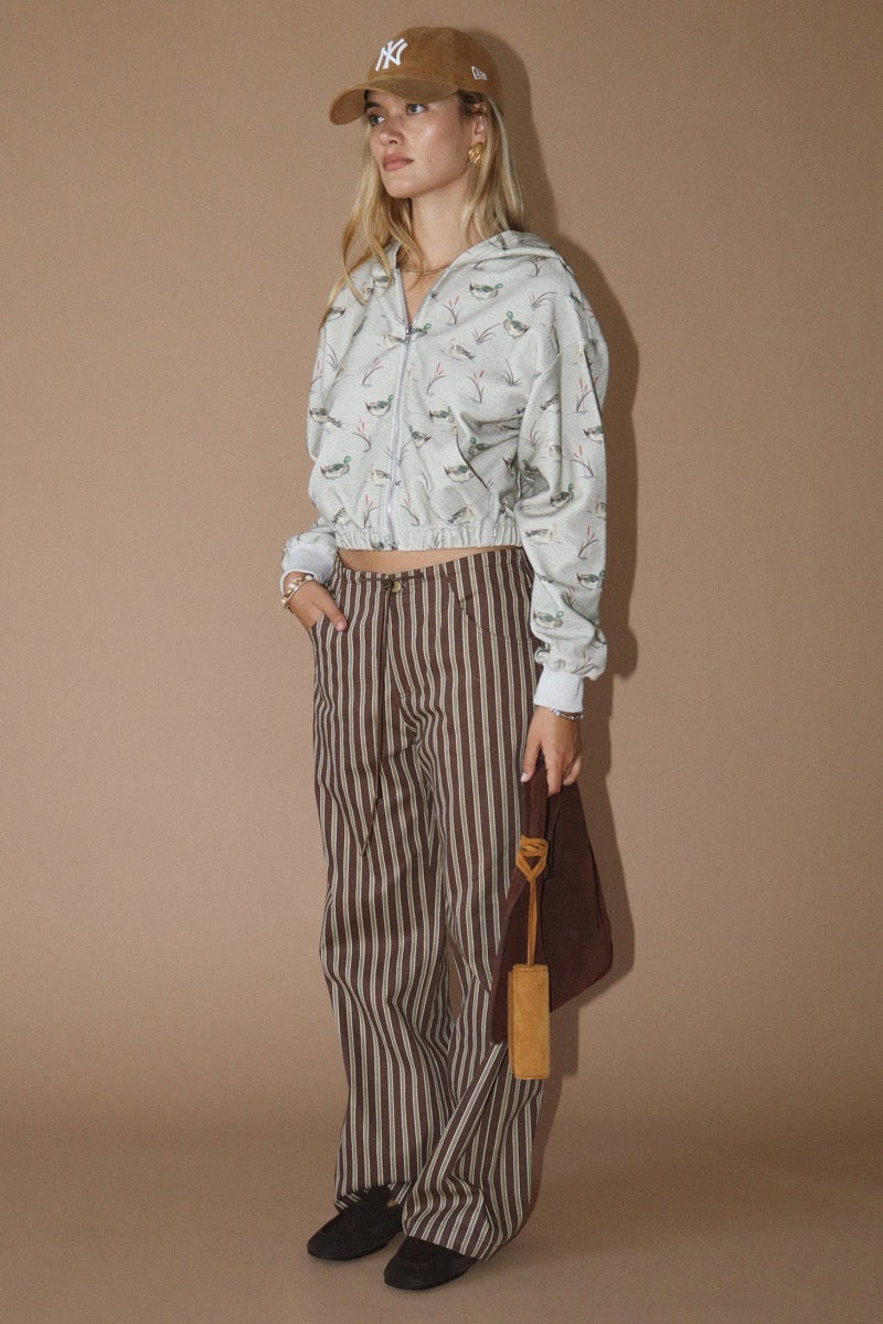 Woman wearing a duck patterned hoodie and striped pants against a beige background