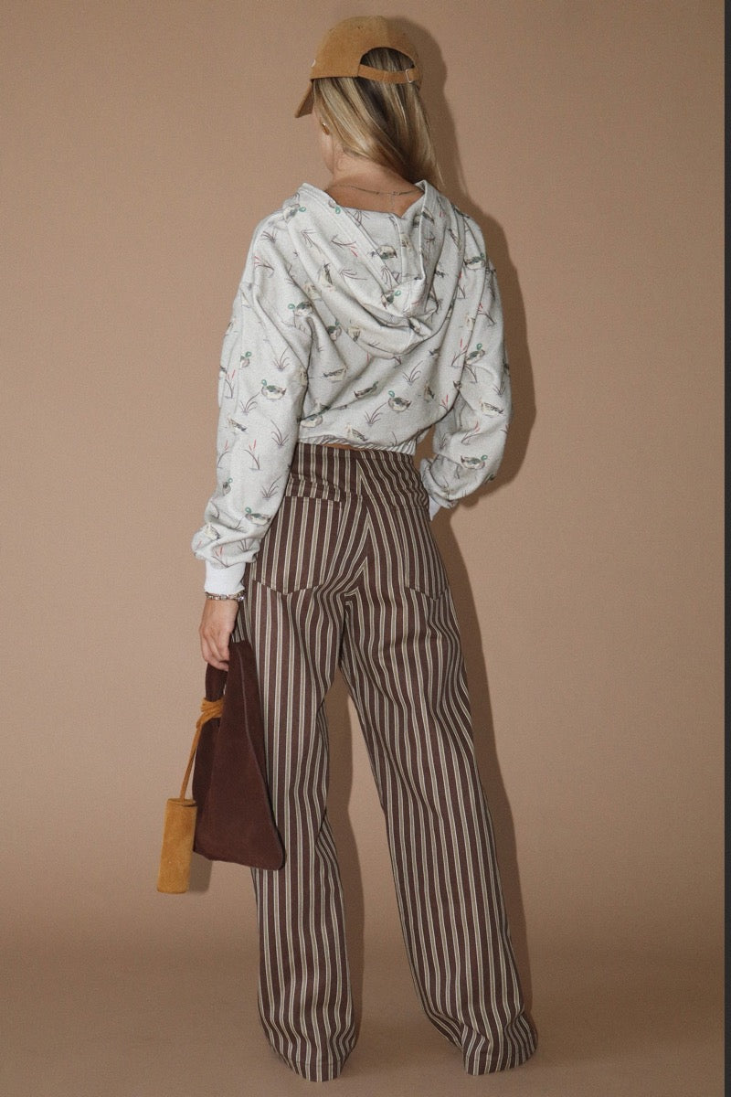 Back view of a woman wearing a duck patterned hoodie and striped pants against a beige background
