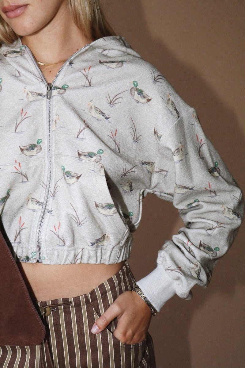 Detail shot of a woman wearing a duck patterned hoodie and striped pants against a beige background