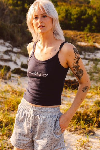 Woman wearing patterned shorts and a navy tank top in a natural setting