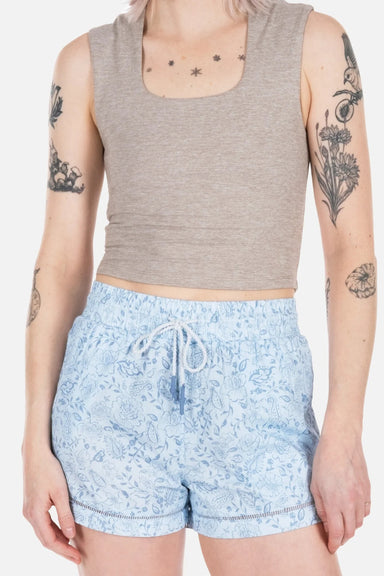 Woman wearing blue patterned shorts with a taupe tank top on a white background