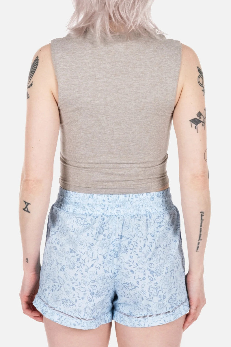 Woman wearing blue patterned shorts with a taupe tank top on a white background