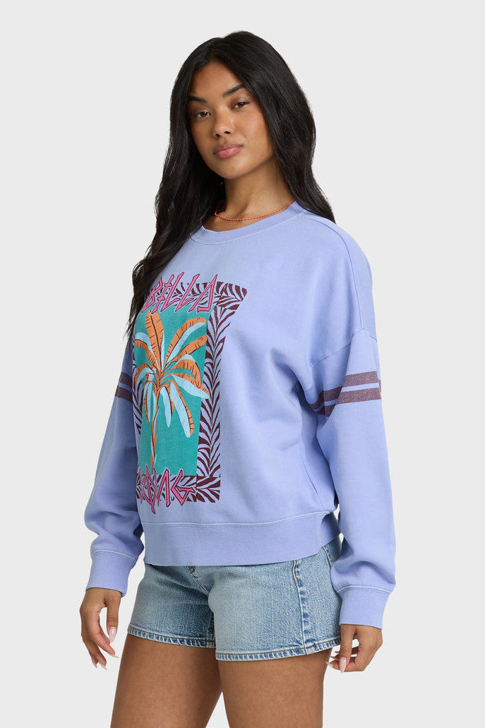 Woman wearing a light blue sweatshirt with a colorful palm tree design on a white background