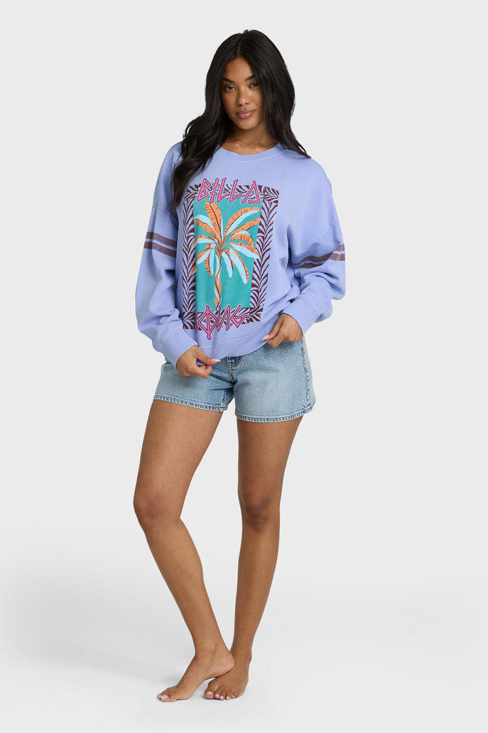 Woman wearing a light blue sweatshirt with a palm tree design and denim shorts on a white background