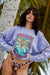 Woman wearing a colorful graphic sweatshirt and patterned shorts in a tropical setting
