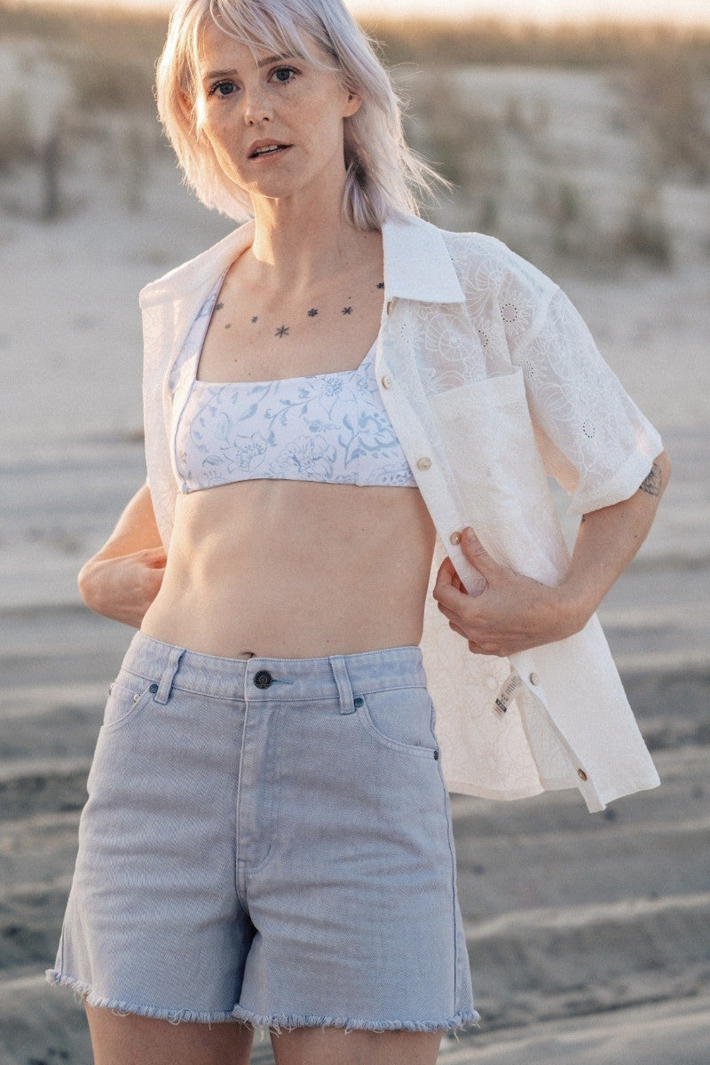 Woman wearing cutoff jean shorts, swim top, and button up shirt on the beach