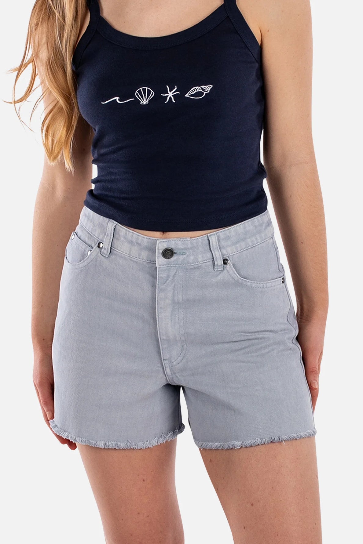 Woman wearing cutoff jean shorts and navy tank top on a white background