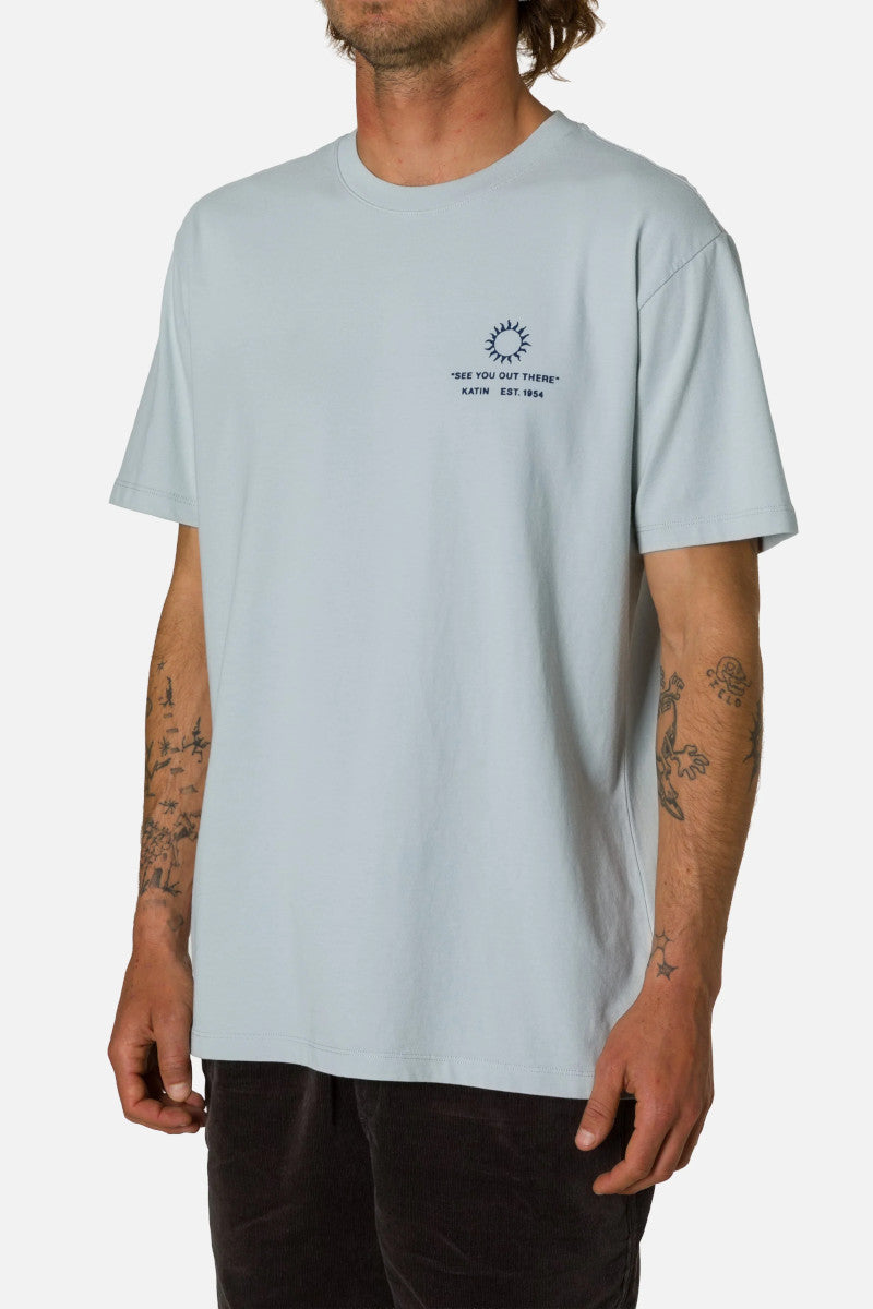 Light blue t-shirt with a small graphic and text worn by a person on a white background