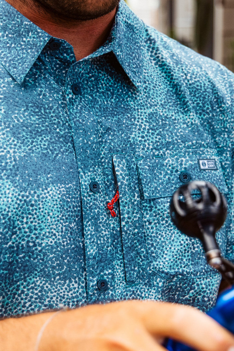Close-up of a person wearing a blue patterned button up shirt with a brand logo on a chest pocket