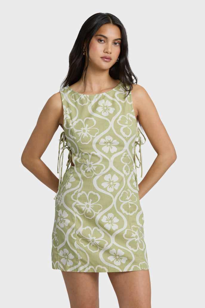 Woman wearing a green and white patterned dress with side ties on a white background